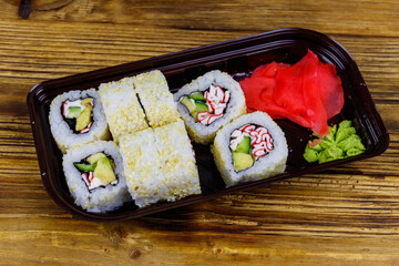 Uramaki sushi rolls with surimi in plastic box on wooden table. Top view. Sushi for take away or delivery of sushi in plastic container