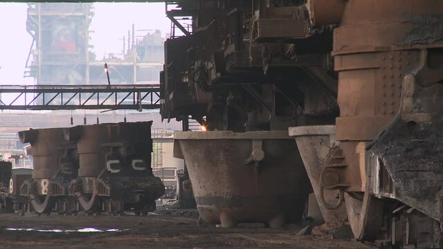 Large slag pots pushed into position by train at industrial steel plant.