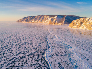 Frozen Lake Baikal, Aerial view. Beautiful winter landscape with clear smooth ice. Famous natural landmark Russia. Blue transparent ice with deep cracks, top view of a frozen lake.