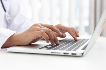 Doctor uses a laptop computer to record patient information and write it on a document to prepare for diagnosis in the room of a modern hospital, Emergency assistance and health care concept.