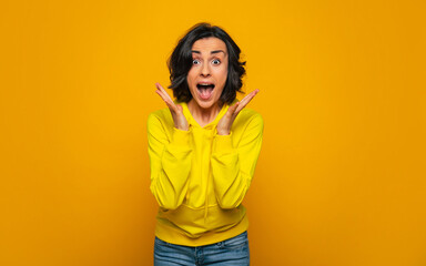 Unexpected win. Half-length photo of excited and happy brunette girl dressed in a yellow hoodie,...