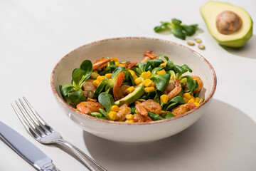 selective focus of fresh green salad with corn, shrimps and avocado on plate near cutlery on white background