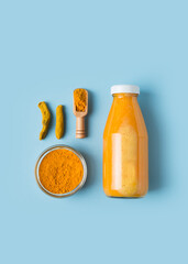 Turmeric smoothie in glass bottle with ingredients, turmeric powder on blue background