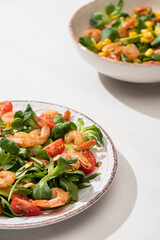 selective focus of fresh green salad with shrimps and avocado on plates on white background