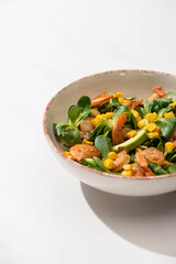 fresh green salad with corn, shrimps and avocado on plate on white background