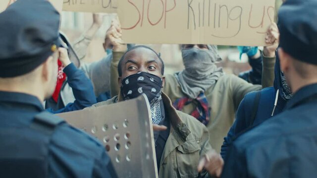Young African American guy protester screaming and shouting at policemen at demonstration for human rights. USA protesters fighting and quarrelling with cops at protest against police violence.