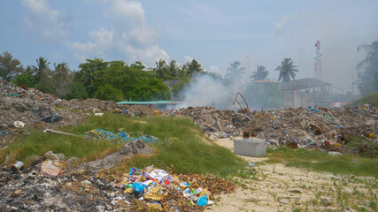 Thick white toxic smoke rolls out of a massive landfill burning plastic garbage.
