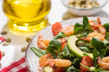 selective focus of fresh green salad with shrimps and avocado on plate and plaid napkin on white background