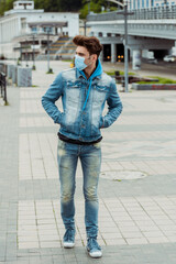 Obraz premium Young man in medical mask and hands in pockets of denim jacket walking on urban street