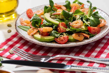 selective focus of fresh green salad with shrimps and avocado on plate near cutlery on plaid napkin