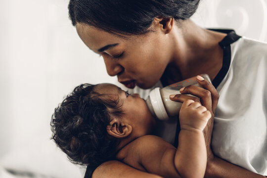 Portrait of enjoy happy love family african american mother playing with adorable little african american baby.Mom feeding bottle of milk to baby cute son in a white  bedroom.Love of black family 