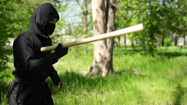 Japanese ninja in a black suit is training with a wooden baton, slow motion