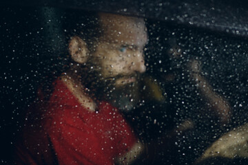 Fototapeta na wymiar Man driver sits at steering wheel of car at rainy night with drops on windshield