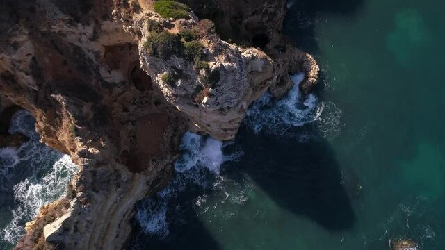 Top down aerial of rough textured and eroded Mediterranean cliffs. waves swirl in the turquoise sea.