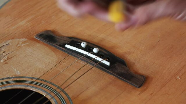 Slow-moving close-up of a man repairing a wooden acoustic guitar. He is using a pair of plyers to remove the sting pins of the maple colored guitar.