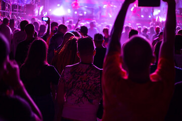 crowd of fans at a rock music concert, young people in the club illuminated by spotlights shoot...