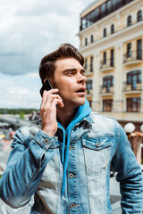 Handsome man in denim jacket talking on smartphone on urban street