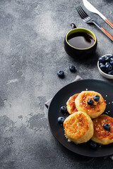 Fritters of cottage cheese with blueberries. Cheese curd cheesecakes, pancakes on a dark concrete background. Copy space.