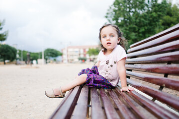 little caucasian girl enjoying a vacation at her beach house. she is sitting on a wooden bench while looking at the camera