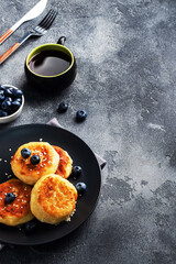Fritters of cottage cheese with blueberries. Cheese curd cheesecakes, pancakes on a dark concrete background. Copy space.
