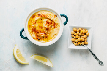 dish of hummus with olive oil and paprika. Next to it there are some lemon slices and a bowl with cooked chickpeas. Image seen from above. Food concept