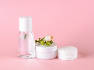Skin tonic lotion or micellar water, facial cream, cotton pads and small rose on a pastel pink background. Cosmetics for moisturizing and cleansing. Skin, hair or body care.