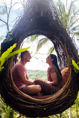 A tourist couple sitting on a large bird nest on a tree at Bali island