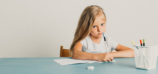 blonde girl sits at a table and writes in a notebook