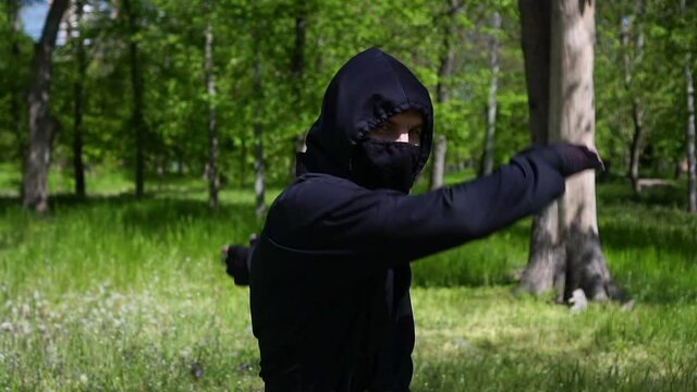 Portrait of a ninja in a black suit. A male ninja is training in the park