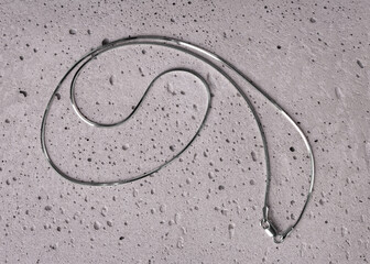 Jewelry chain made of white metal close-up. Thin chain of platinum on a stone gray background.