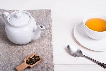 Teapot on linen napkin, a portion of green tea to brew a cup of tea and a spoon on the table