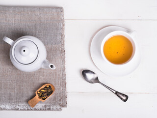 Teapot on linen napkin, a portion of green tea to brew a cup of tea and a spoon on the table