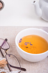 A teapot, a cup of green tea and candy in a shaded metal vase and a rolled-up warm plaid and glasses on a white wooden table - the concept of home comfort
