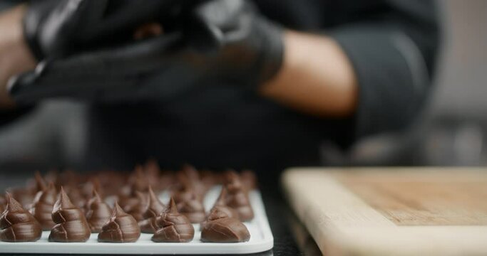 Chef chocolatier in black gloves rolls up small candies from self cooked chocolate in slow motion, making the truffles, cooking the sweet desserts from chocolate and cocoa, making candies, 4k DCI 120