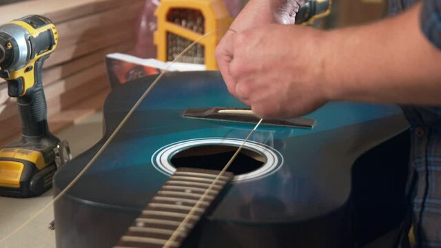 A man restoring a blue guitar grabs a new string and string knob and begins restringing the guitar.