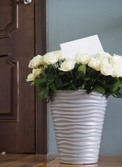 There is a large bouquet of white roses in a vase by the door.Space for text.Holiday greetings.