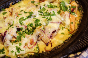 Close up view of delicious baked meal, that conains of mushroms, fish, onion, cheese. Restaurant menu.