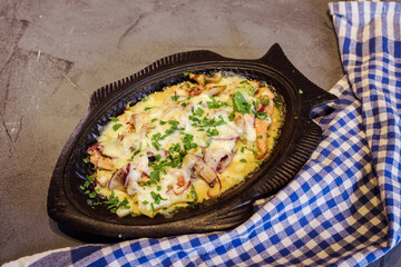 Delicious hot meal made of salmon fish, mushrooms, onion and parsley, coverd with cheese and baked in the oven in fish shape. Grey baclkground, blue and white plaid towel.