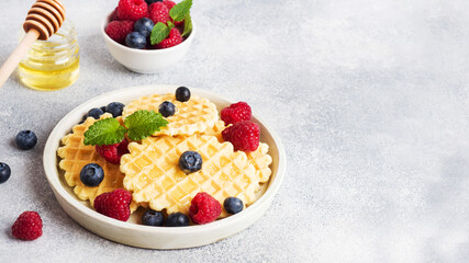 Corrugated waffle cookies with fresh raspberries and blueberries on a concrete background. Copy space.