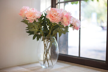 Pink peonies stand in a glass vase on a windowsill