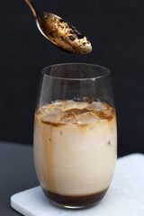 iced coffee with milk and ice in a transparent glass on a marble board on a dark background, summer coffee drink