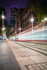 Long exposure of a cable car tram light rail carriage speeding past in the night time along a busy city street