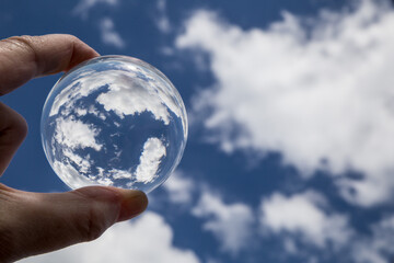 Hand hält Glaskugel mit blauem Himmel mit Wolken