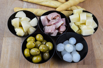 Italian appetizers with green olives, spring onions, porchetta ham, fontina cheese, smoked provola cheese and breadsticks close up
