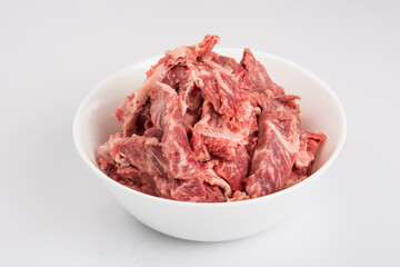 isolated close up corner shot of sliced raw beef fillet pieces in a white bowl on a white background