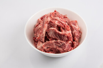 isolated close up top view shot of sliced raw beef fillet pieces in a white bowl on a white background