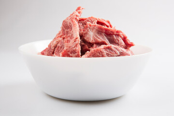 isolated close up side view shot of sliced raw beef fillet pieces in a white bowl on a white background