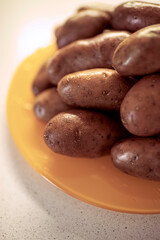Whole raw potatoes in a peel on an orange plate.