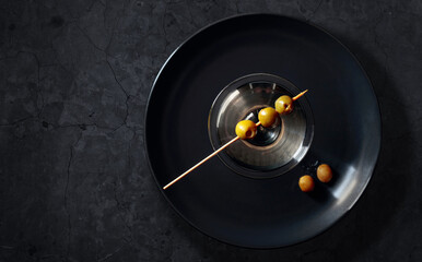 Obraz premium Dry martini with green olives on a black stome table.