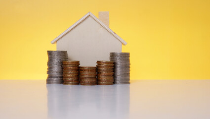 Mini wooden house with stacking coins on yellow background. Conceptual saving image.